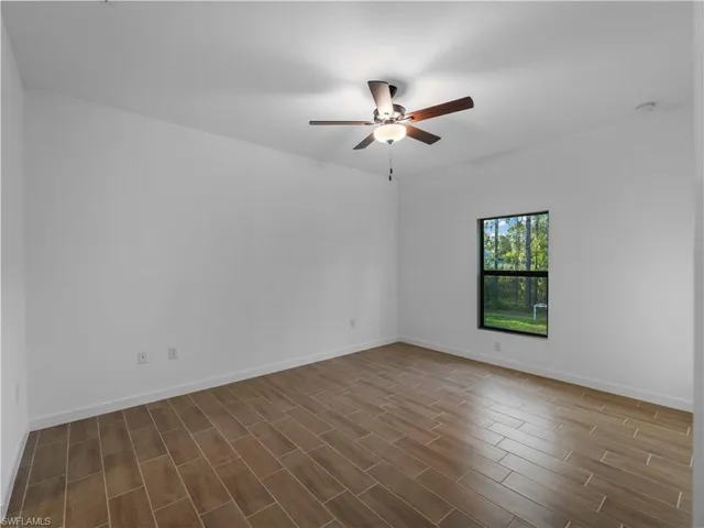 Unfurnished room with a ceiling fan, dark wood-style flooring, baseboards, and a smoke detector
