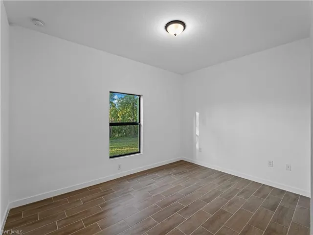 Empty room with dark wood-style floors, a smoke detector, and baseboards