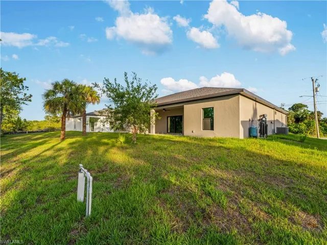 Rear view of house featuring stucco siding, central air condition unit, a lawn, and ceiling fan
