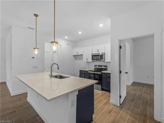 Kitchen with stainless steel appliances, a sink, wood tiled floors, white cabinetry, and recessed lighting