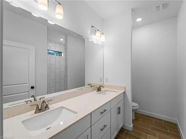 Full bathroom with toilet, wood finish floors, baseboards, double vanity, and recessed lighting