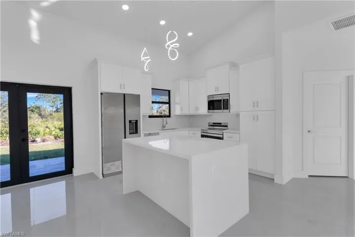 Kitchen with pendant lighting, a center island, high vaulted ceiling, white cabinetry, and stainless steel appliances