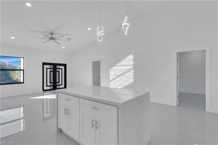 Kitchen with vaulted ceiling, ceiling fan, decorative light fixtures, white cabinets, and a kitchen island