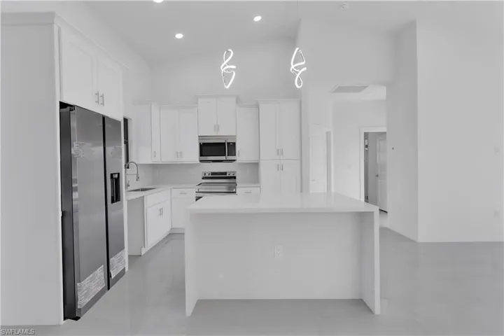 Kitchen with decorative light fixtures, a center island, white cabinetry, and stainless steel appliances