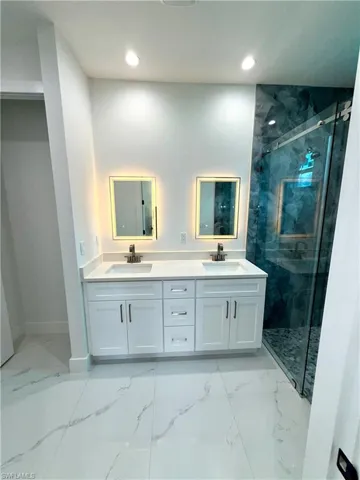 Full bath featuring marble look tile flooring, a marble finish shower, double vanity, and recessed lighting