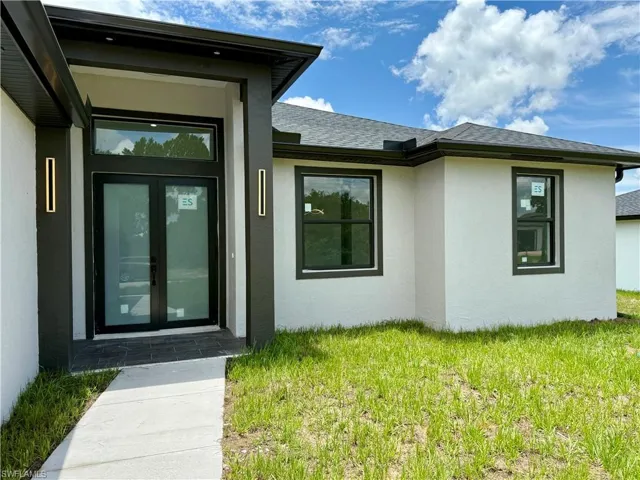 Doorway to property with stucco siding, a yard, french doors, and a shingled roof