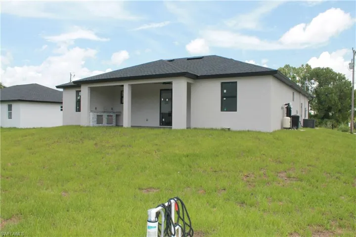 Rear view of property featuring a yard, stucco siding, and a shingled roof