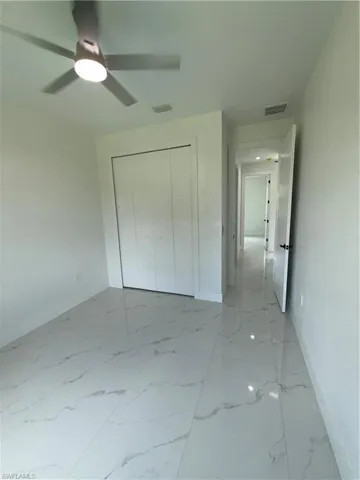 Unfurnished bedroom featuring a closet, light marble finish flooring, and ceiling fan