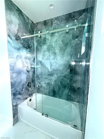 Bathroom featuring enclosed tub / shower combo and marble look tile flooring