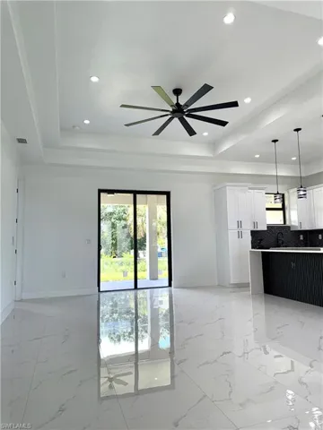 Unfurnished living room featuring a raised ceiling, recessed lighting, a ceiling fan, and light marble finish floors