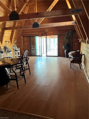 Dining area featuring hardwood / wood-style floors, vaulted ceiling with beams, and wooden walls