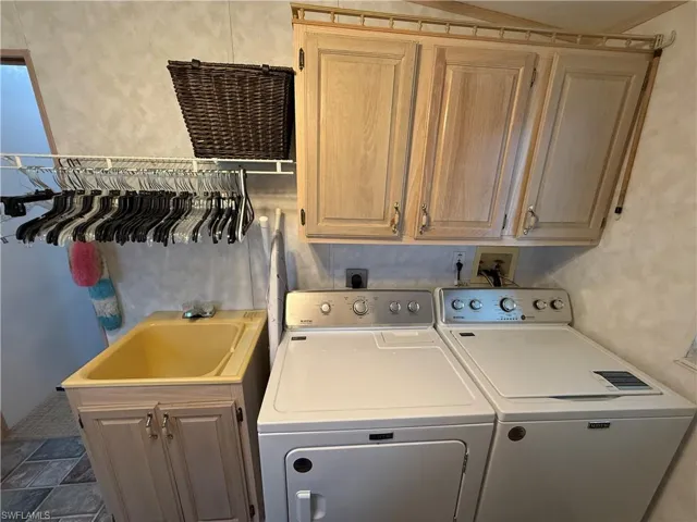 Clothes washing area featuring sink, cabinets, and washer and clothes dryer