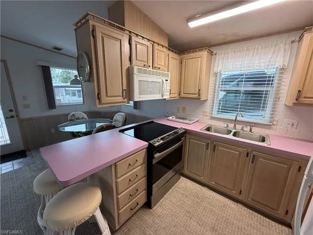Kitchen featuring stainless steel electric stove, lofted ceiling, sink, wood walls, and a breakfast bar area