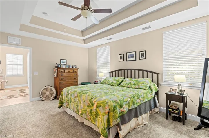 Bedroom featuring a raised ceiling, light carpet, and ceiling fan