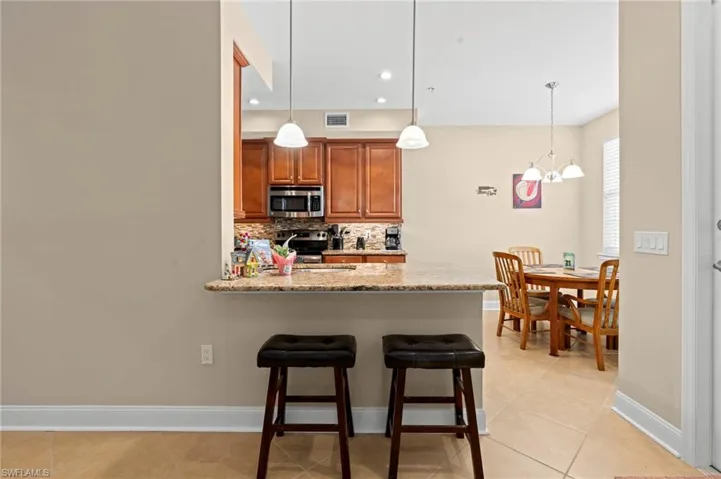 Kitchen with tasteful backsplash, brown cabinets, light stone countertops, a kitchen breakfast bar, and light tile patterned flooring