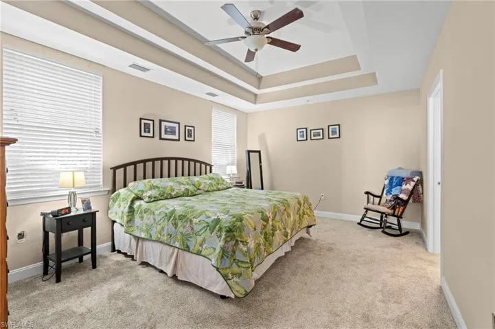 Bedroom with light carpet, ceiling fan, and a tray ceiling