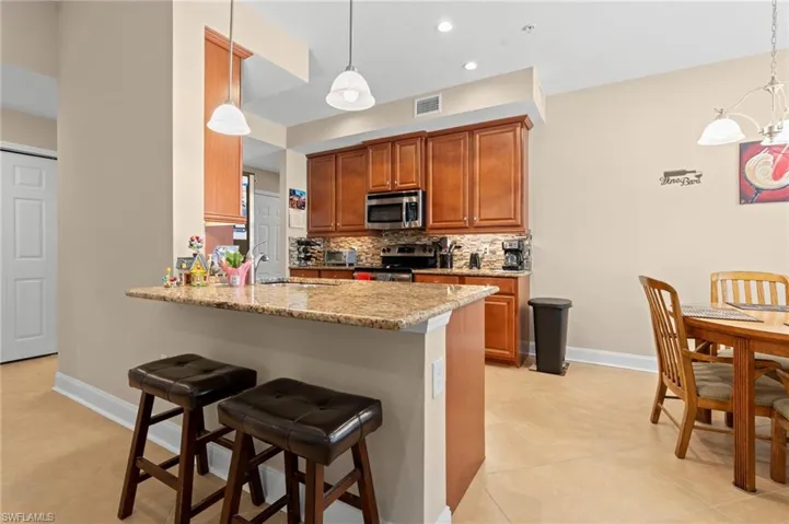 Kitchen with decorative backsplash, a breakfast bar, light stone countertops, a peninsula, and brown cabinetry