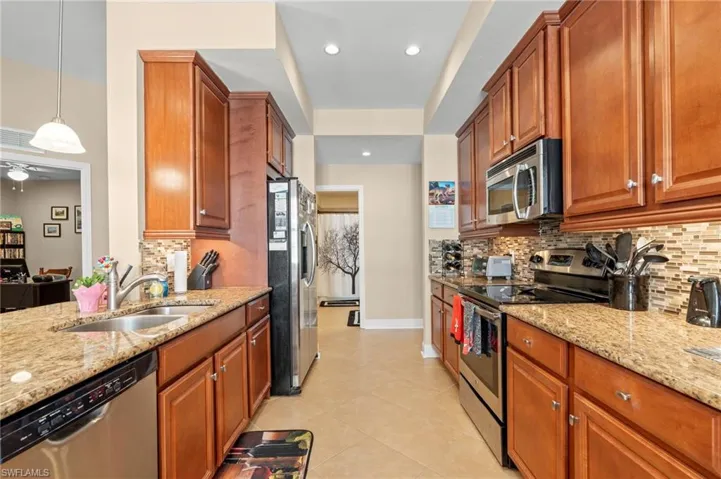 Kitchen featuring appliances with stainless steel finishes, light stone counters, brown cabinets, and recessed lighting