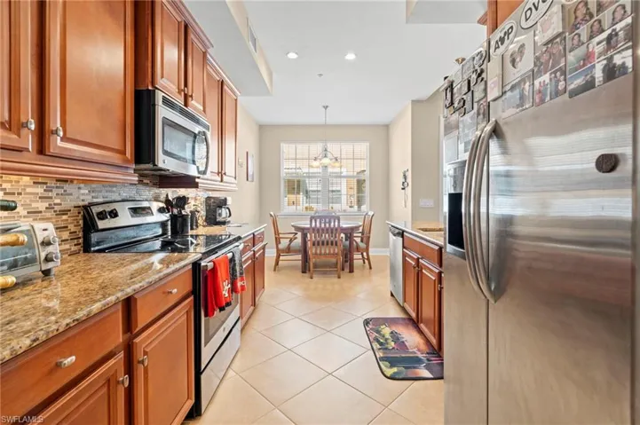 Kitchen with appliances with stainless steel finishes, brown cabinets, light stone counters, and recessed lighting