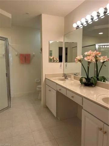 Bathroom featuring dual bowl vanity, toilet, tile floors, an enclosed shower, and a textured ceiling