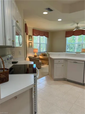 Kitchen featuring light tile flooring, dishwasher, stove, ceiling fan, and white cabinets