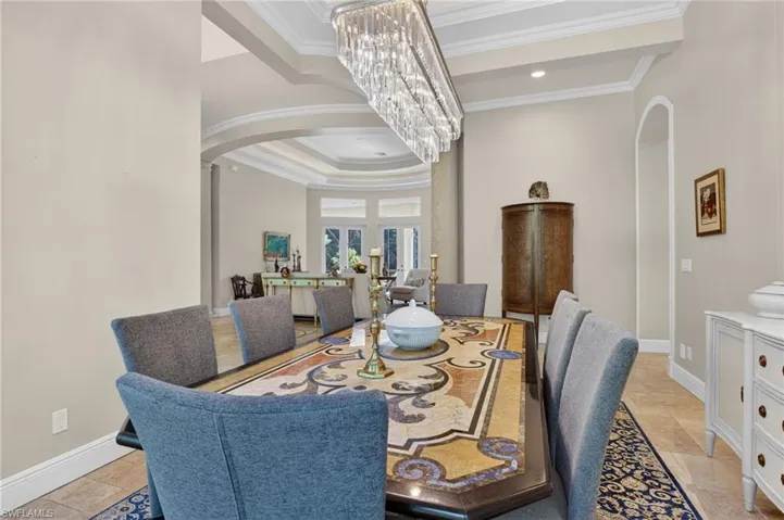 Dining space with arched walkways, crown molding, a tray ceiling, ornate columns, and a chandelier
