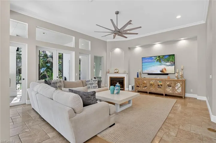 Living area featuring a glass covered fireplace, a ceiling fan, ornamental molding, stone tile floors, and recessed lighting