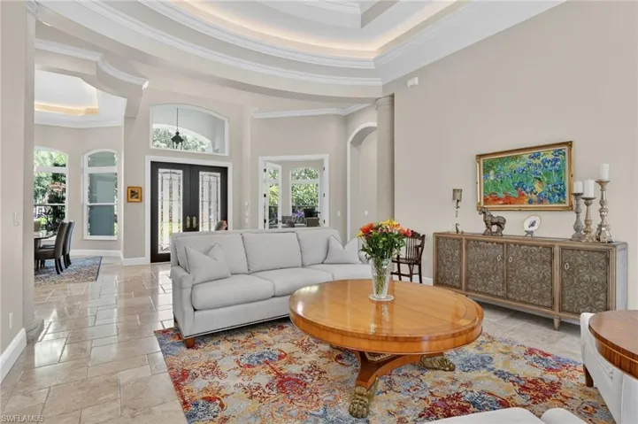 Living area featuring a towering ceiling, a tray ceiling, decorative columns, stone tile floors, and french doors