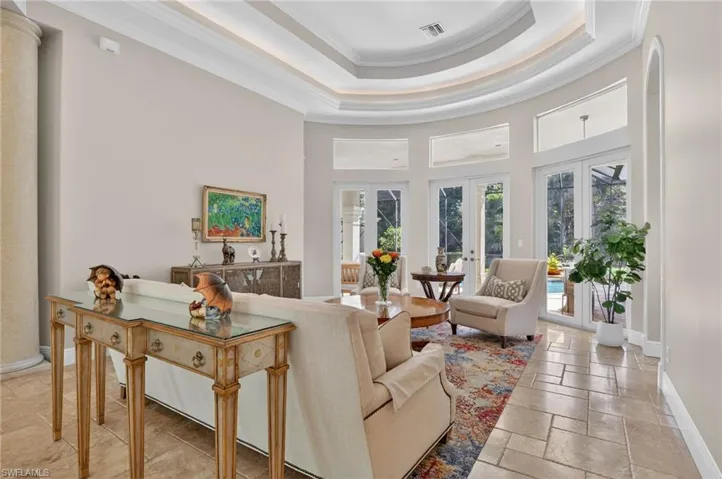 Living area featuring ornamental molding, a high ceiling, french doors, stone tile flooring, and a raised ceiling