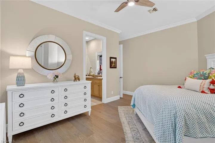 Bedroom with ensuite bathroom, light wood-style floors, ornamental molding, and ceiling fan