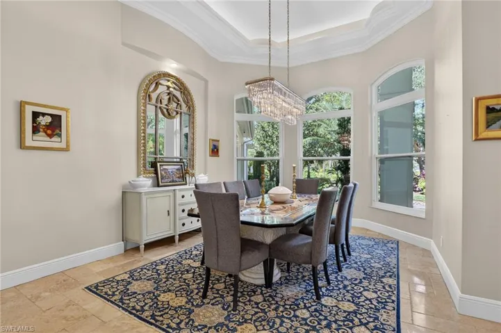Dining space with crown molding, a chandelier, a tray ceiling, and stone tile flooring