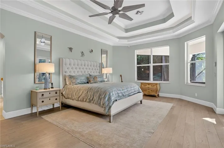 Bedroom with crown molding, light wood finished floors, ceiling fan, and a raised ceiling