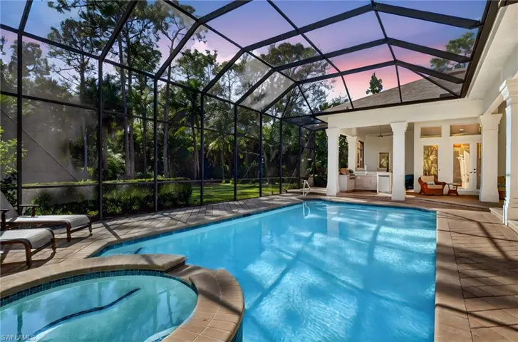 Pool at dusk with glass enclosure, a pool with connected hot tub, a sunroom, a patio, and an outdoor hangout area