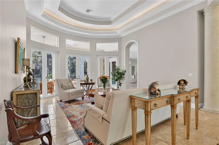 Living room featuring crown molding, french doors, a towering ceiling, arched walkways, and stone tile flooring