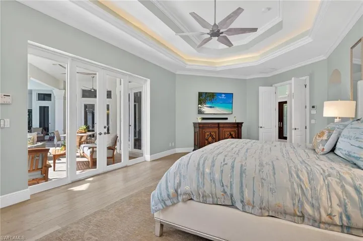 Bedroom featuring french doors, a tray ceiling, ornamental molding, access to exterior, and ceiling fan