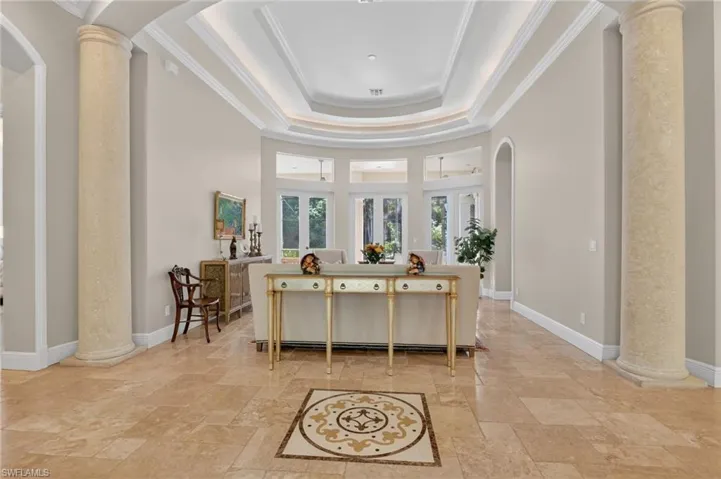 Foyer featuring ornate columns, arched walkways, ornamental molding, stone tile flooring, and a tray ceiling