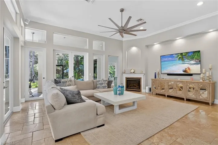 Living area with crown molding, ceiling fan, a glass covered fireplace, stone tile flooring, and recessed lighting