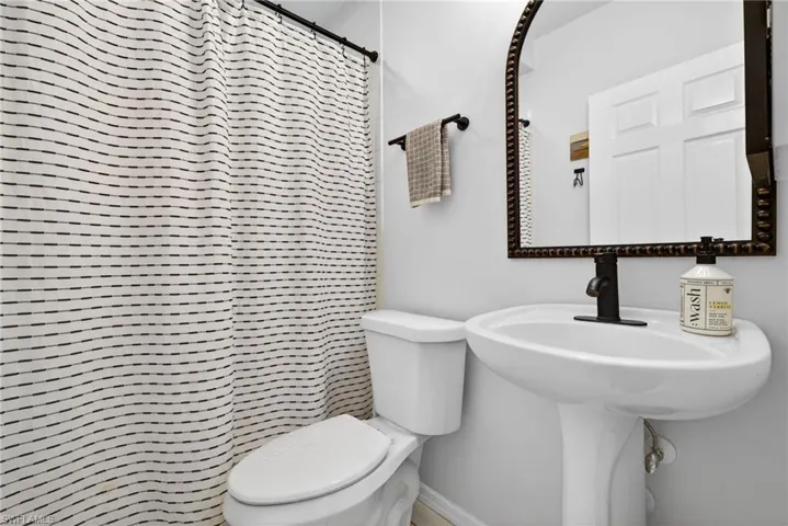 Bathroom featuring a pedestal sink with a matte black faucet, a framed mirror, and a white toilet