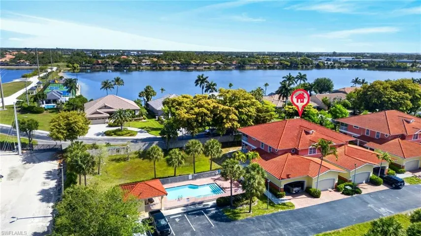 Waterfront property featuring a red tile roof, an attached garage, mature palm trees, and a community pool