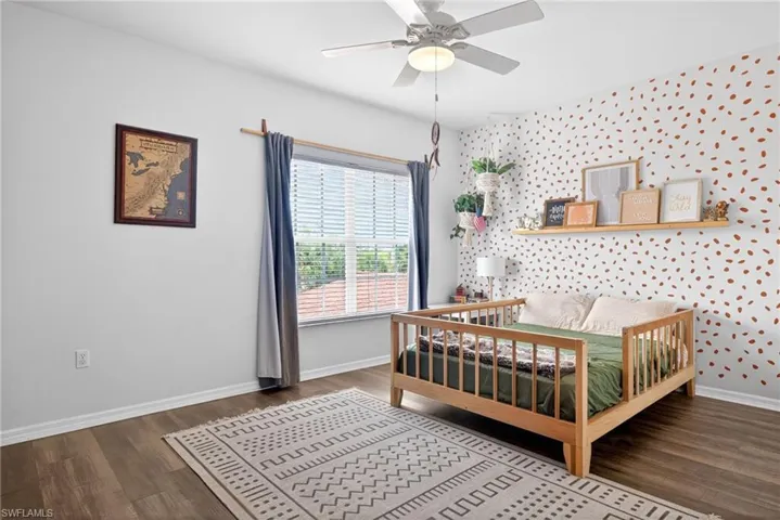Room featuring wood-finish flooring, a ceiling fan with integrated lighting, a window with horizontal blinds, and a built-in wall shelf