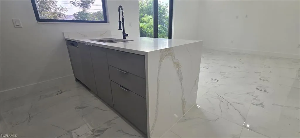 Kitchen view of modern cabinets, a peninsula, gray cabinetry, light stone counters, and dishwasher
