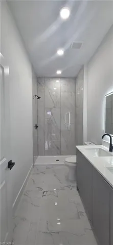 Bathroom featuring a marble finish shower, vanity, light marble finish flooring, and recessed lighting