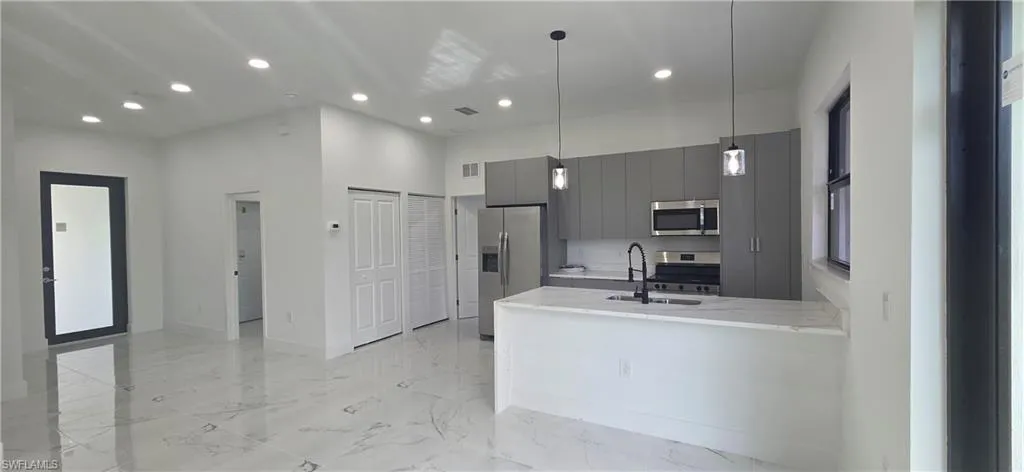 Kitchen with modern cabinets, recessed lighting, gray cabinets, appliances with stainless steel finishes, and light stone counters