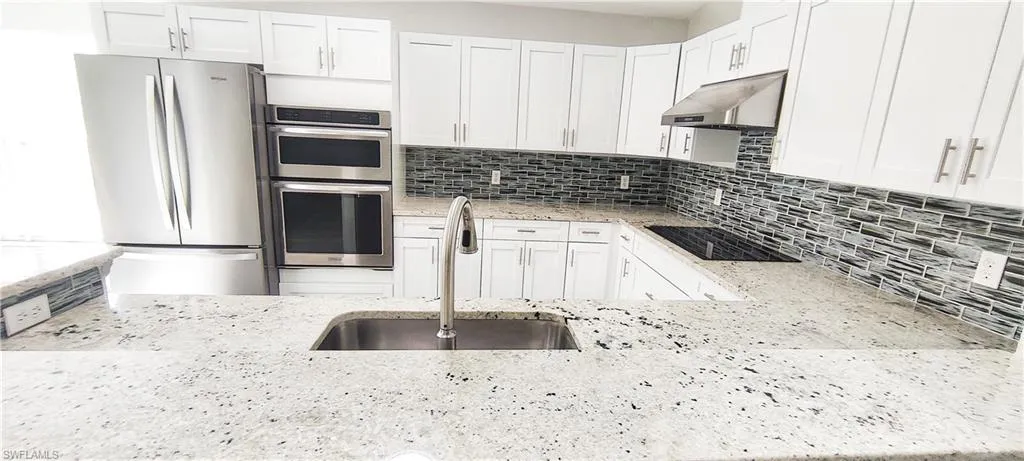 Kitchen with sink, light stone counters, white cabinets, and appliances with stainless steel finishes