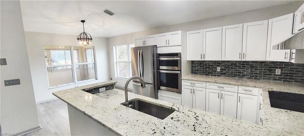 Kitchen featuring light stone countertops, white cabinets, appliances with stainless steel finishes, decorative light fixtures, and sink