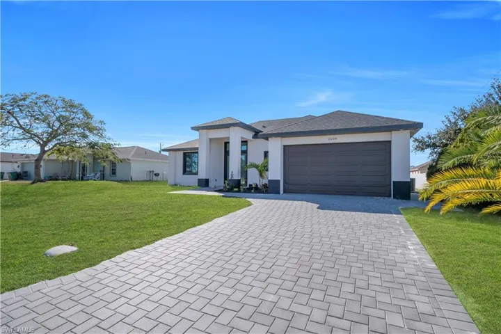 Prairie-style house featuring decorative driveway, a front yard, an attached garage, and stucco siding