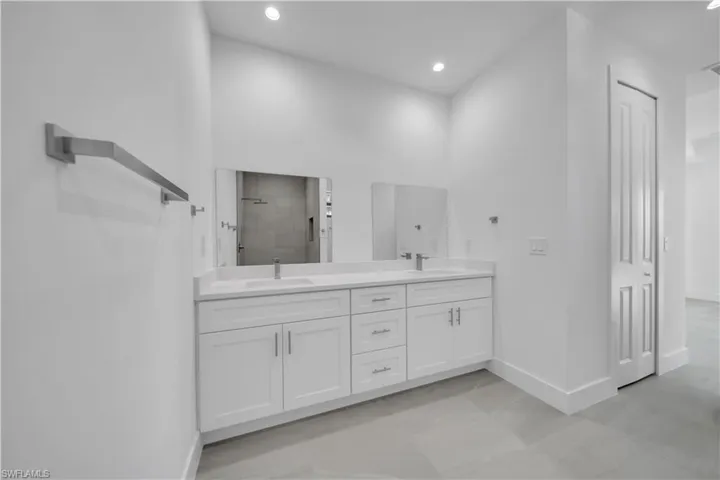 Full bath featuring double vanity, tiled shower, recessed lighting, and a spacious closet