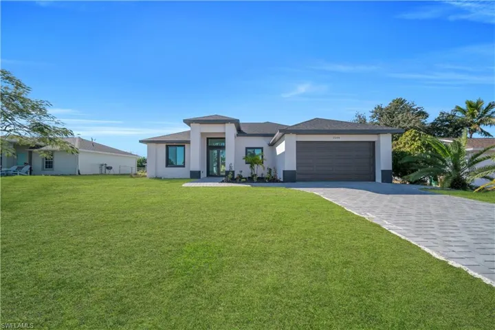 Prairie-style house featuring a front yard, decorative driveway, stucco siding, and an attached garage