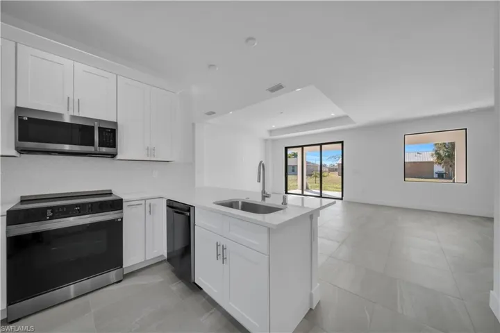 Kitchen with electric range oven, white cabinets, a raised ceiling, stainless steel microwave, and light stone counters