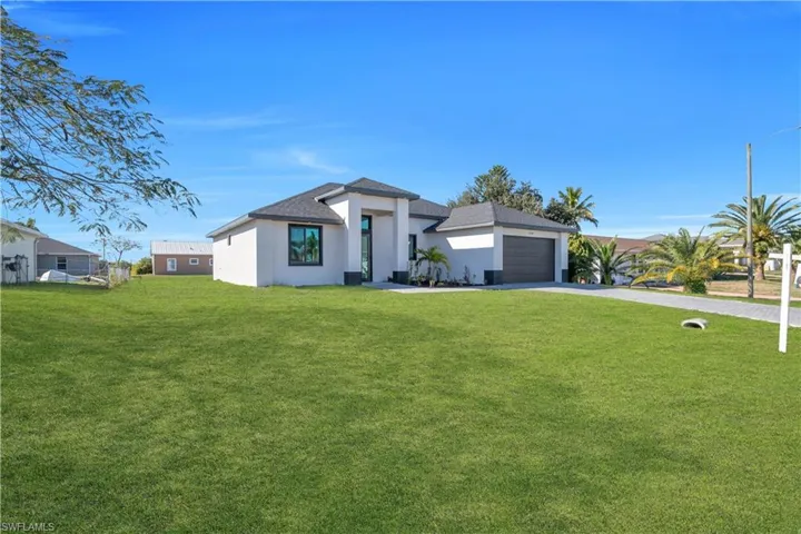 Prairie-style home featuring a front yard, stucco siding, driveway, a garage, and a shingled roof